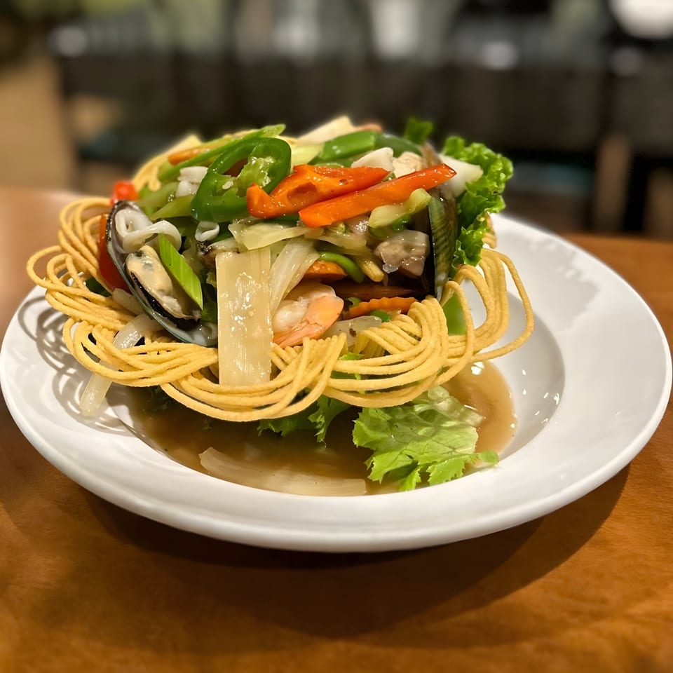 Crispy noodle basket filled with colorful stir-fried vegetables, shrimp, and mussels in a savory sauce.