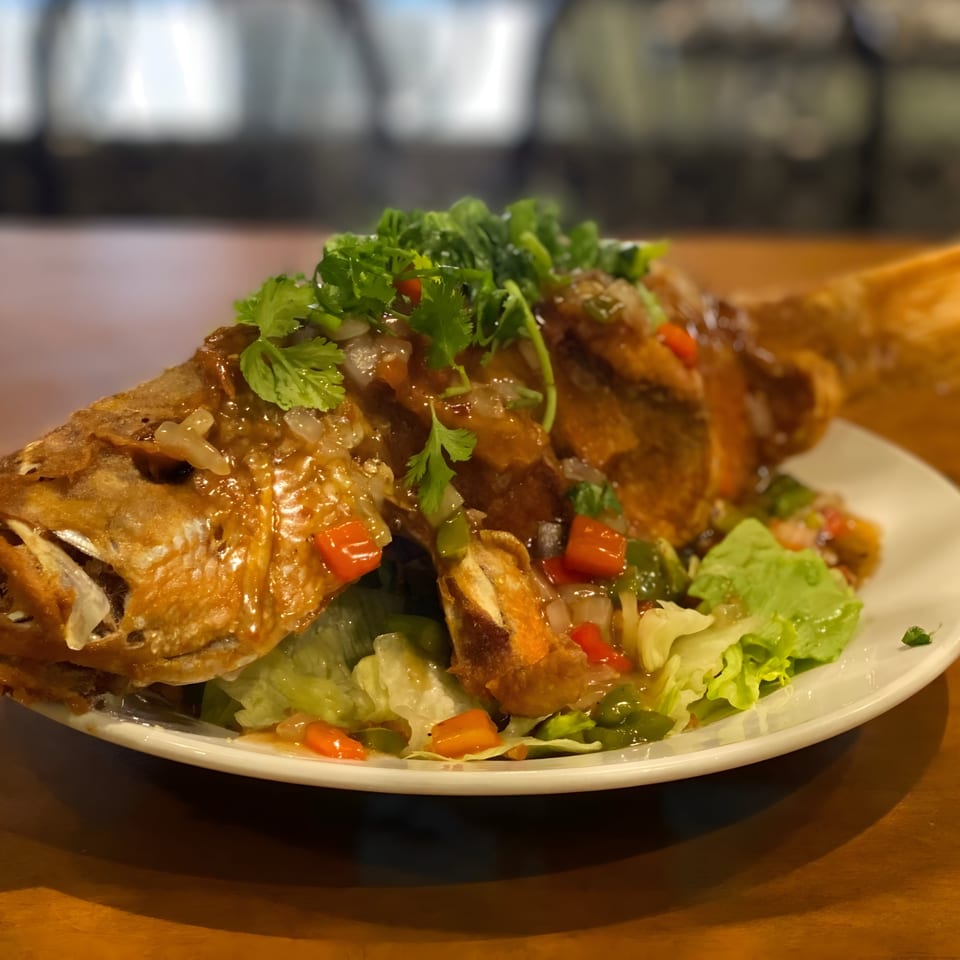 Whole fried fish with sweet chili sauce, bell peppers, onions, and cilantro on a bed of lettuce.