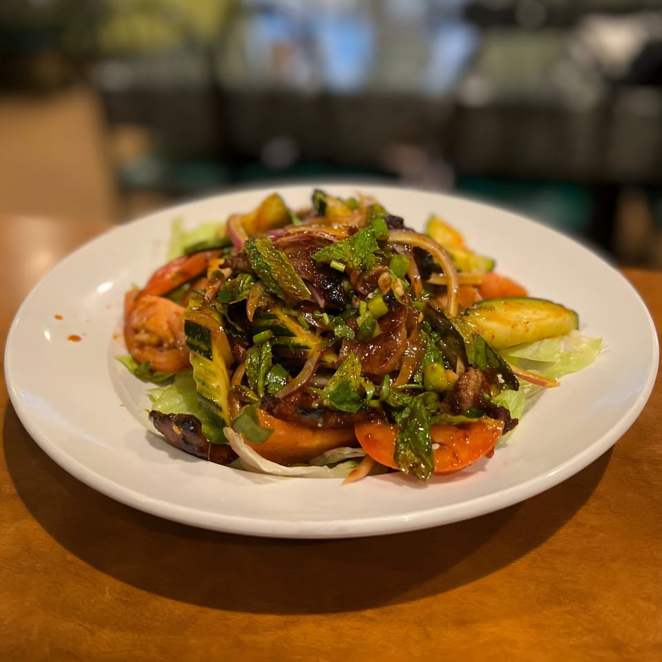 Thai salad with grilled beef, red onions, tomatoes, cucumbers, mint, and a dark sauce.
