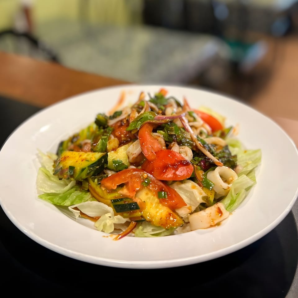 Thai Orchid's spicy seafood salad with squid, tomatoes, and greens on a white plate.