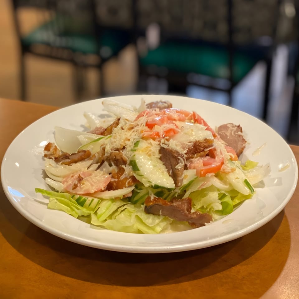 Thai salad with sliced meat, lettuce, tomatoes, cucumbers, and onions, topped with dressing and cheese.