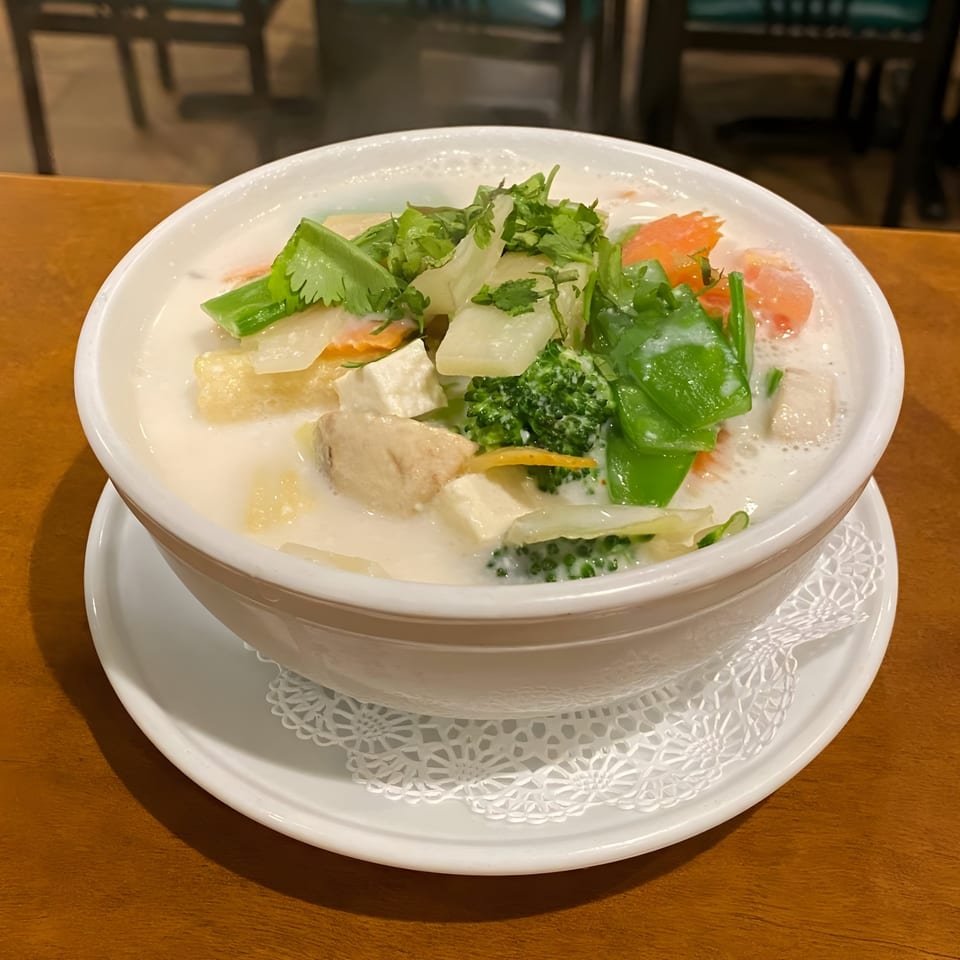 Creamy Thai soup with tofu, broccoli, carrots, and cilantro in a white bowl on a wooden table.